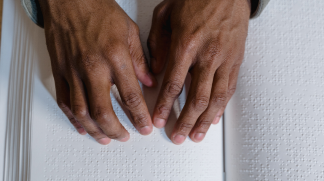 Two hands touching braille dots on an open book