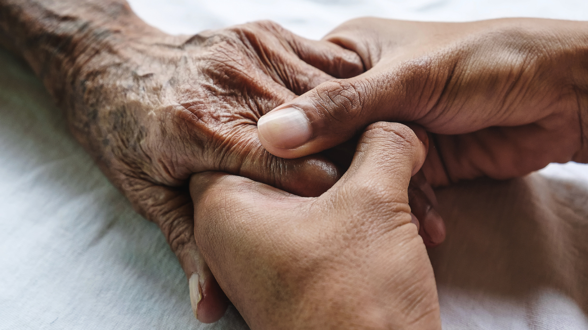 Patient's hand being held by medical carer. 